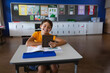© WavebreakMediaMicro - Child boy sitting at student desk in bright classroom, holding tablet with open workbook and pencil