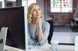 © wavebreak3 - Woman gazing thoughtfully past desktop monitor in open-plan office, with keyboard papers coffee cup