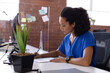 © wavebreak3 - Diverse woman writing in notebook at open-plan office desk with monitor and succulent, copy space
