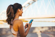 © Dragana Gordic - Young Woman Using Smartphone and Earbuds Outdoors Near a Modern Bridge
