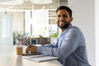 © WavebreakMediaMicro - Man smiling and sitting at desk in office with laptop, pen and coffee cup, copy space