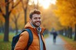 © miss irine - Smiling young man with backpack enjoys autumn day in park. Happy traveler walks outdoors in fall season, yellow leaves trees background. Leisure activity in city.