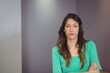 © WavebreakMediaMicro - Female standing with arms crossed indoors against smooth grey panel walls, with neutral expression