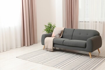 Poster - Stylish living room interior with cozy sofa, houseplant and elegant curtains