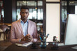 © Wavebreak Media - Young African American man sitting at desk in open?plan office, with notebooks, pens and coffee cup