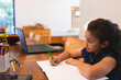 © Wavebreak Media - bi-racial girl child writing at home study table using green pencil with laptop, copy space
