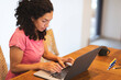 © Wavebreak Media - Woman typing on laptop at wooden table in cozy home, with coffee mug and colored pencils