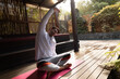 © Wavebreak Media - Young adult man stretching torso on pink yoga mat on wooden deck under pergola, copy space