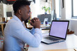 © Wavebreak Media - African American man sitting at desk in modern office, working with laptop, notebook, copy space
