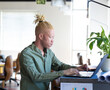 © Wavebreak Media - African American man typing at laptop in modern office space with potted plant and rolled papers
