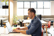 © Wavebreak Media - Man typing on laptop at open-plan office desk, using notebook next to coffee and potted plant