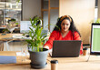 © Wavebreak Media - Woman working on laptop at desk in open-plan office, with coffee cups and potted plant