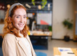 © Wavebreak Media - Woman smiling at camera in modern open plan office with desks monitors and plant, copy space