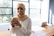 © Wavebreak Media - Indian woman standing in modern office, holding ceramic mug with laptop and plans, smiling