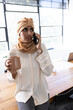 © Wavebreak Media - Indian woman speaking on smartphone and holding mug at table in office, with multi-pane window