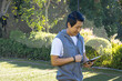 © Wavebreak Media - Mid-adult Asian man tapping tablet on green turf field by black net fence, copy space