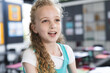 © Wavebreak Media - 8-year-old girl smiling and talking in class, with desks chairs cabinets and bulletin board posters