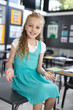 © Wavebreak Media - Female child sitting on student desk in school classroom, showing colorful notebooks and posters
