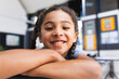 © Wavebreak Media - Schoolgirl leaning on desk in classroom, smiling at camera with educational displays