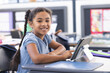 © Wavebreak Media - 8-year-old girl sitting at school desk using tablet in classroom with notebook and folder