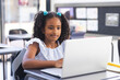 © Wavebreak Media - Girl working on laptop at classroom desk with black chair, notebooks, pencils and striped backpack