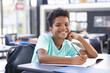 © Wavebreak Media - Child boy sitting at school desk in classroom, writing in notebook with pencil and backpack hanging