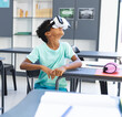 © Wavebreak Media - Multiracial boy learning through white VR headset at desk in bright classroom, with pink headphones