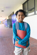© Wavebreak Media - Diverse boy standing and smiling in school corridor with red binder and blue-white striped backpack