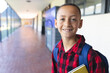 © Wavebreak Media - Diverse school-age boy standing in school hallway with yellow book and blue backpack, copy space