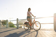 © Wavebreak Media - Asian Korean woman riding orange bicycle on waterfront promenade, with metal guardrails and walkway