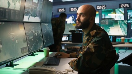 Poster - Military soldier in mission control center overseeing national safety operations with devices, close up. Middle Eastern army specialist examining data in monitoring room command center, camera B