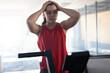 © Wavebreak Media - Woman standing on treadmill in well-lit gym, catching breath with hands on head and console visible
