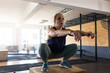 © Wavebreak Media - Woman squatting on wooden plyometric box at indoor gym with squat racks, extending arms for balance