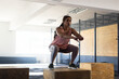© Wavebreak Media - Woman squatting on wooden plyometric box in industrial style gym, with metal pull up rig