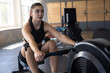 © Wavebreak Media - woman using rowing machine in indoor gym with large windows, showing kinesiology tape on thigh