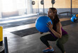 © Wavebreak Media - Woman squatting with blue medicine ball in warehouse gym with weight racks, rubber mats, copy space