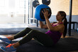 © Wavebreak Media - Woman performing Russian twist on black exercise mat in gym, gripping blue and black medicine ball