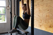 © Wavebreak Media - Young woman performing hanging leg-raise in home gym space, with pull-up bar and wooden wall panel