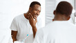 © Prostock-studio - Handsome African American Man Touching Face After Shaving Standing Near Mirror In Modern Bathroom At Home. Male Beauty Morning Routine, Facial Skincare And Self-Care Cosmetics Concept. Panorama