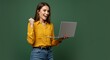 © Muaz - Woman in yellow shirt and jeans celebrates success while holding a laptop on a green background