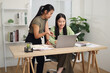 © Johnstocker - Portrait of Asian woman is standing writing in a notebook while discussing ideas with a colleague sitting in front of a laptop.