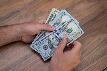 Poster - Male entrepreneur hands hold various dollar banknotes preparing right quantity of cash for paying monthly salary to seasonal worker sitting at workplace in office