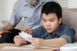 © wichayada - Focused Learning and Family Connection. A grandson examines educational materials while his grandfather offers guidance.