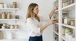 © Firman Dasmir - Young woman arranging food containers in a minimalist pantry with a clean white aesthetic