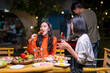 © Wasana - A group of people are eating food together, with one woman eating a hot dog