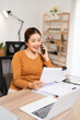 © Fahng - Calling clients on a mobile phone. Professional business woman looking at a paper document while talking on a phone call. Young business woman working in home office.