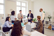 © Studio Romantic - Group of multicultural business people in the office listening to a colleague with a report. Male employee stands with a document, colleagues are looking at him. Concept agenda, teamwork