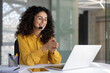 © Liubomir - A cheerful customer service representative wearing a headset smiles while working on her laptop. The woman is in a modern office.