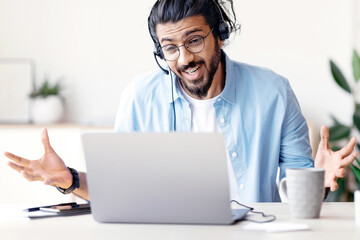 Poster - Joyful Arab Man In Headset Having Web Conference On Laptop In Office, Cheerful Eastern Guy Making Video Call With Computer, Sitting At Desk Talking And Gesturing At Camera, Free Space