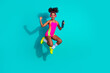 © deagreez - Young woman in colorful activewear performing an energetic jump with posed gestures against a teal background